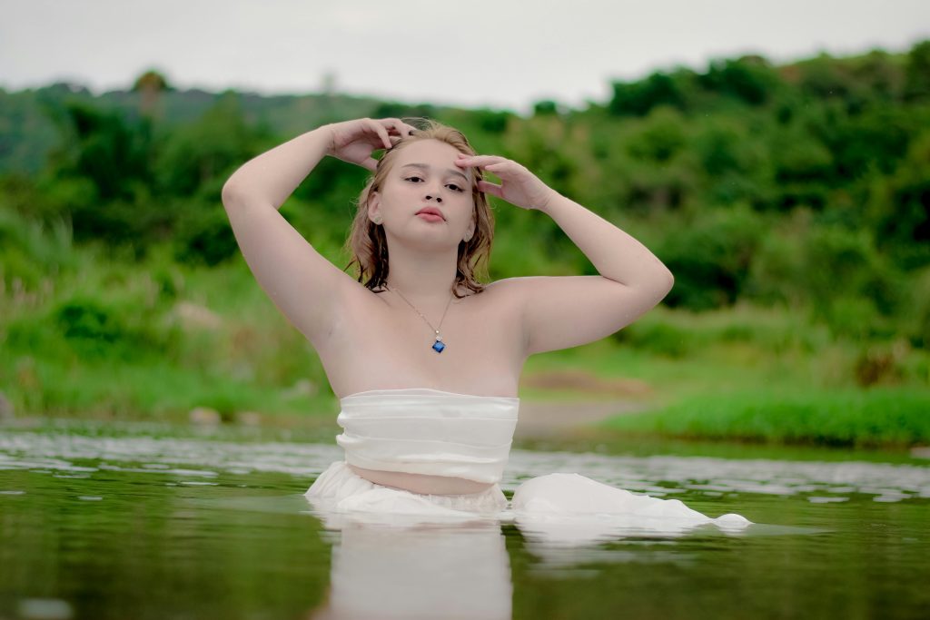A serene woman in a tube top poses gracefully in lush nature.