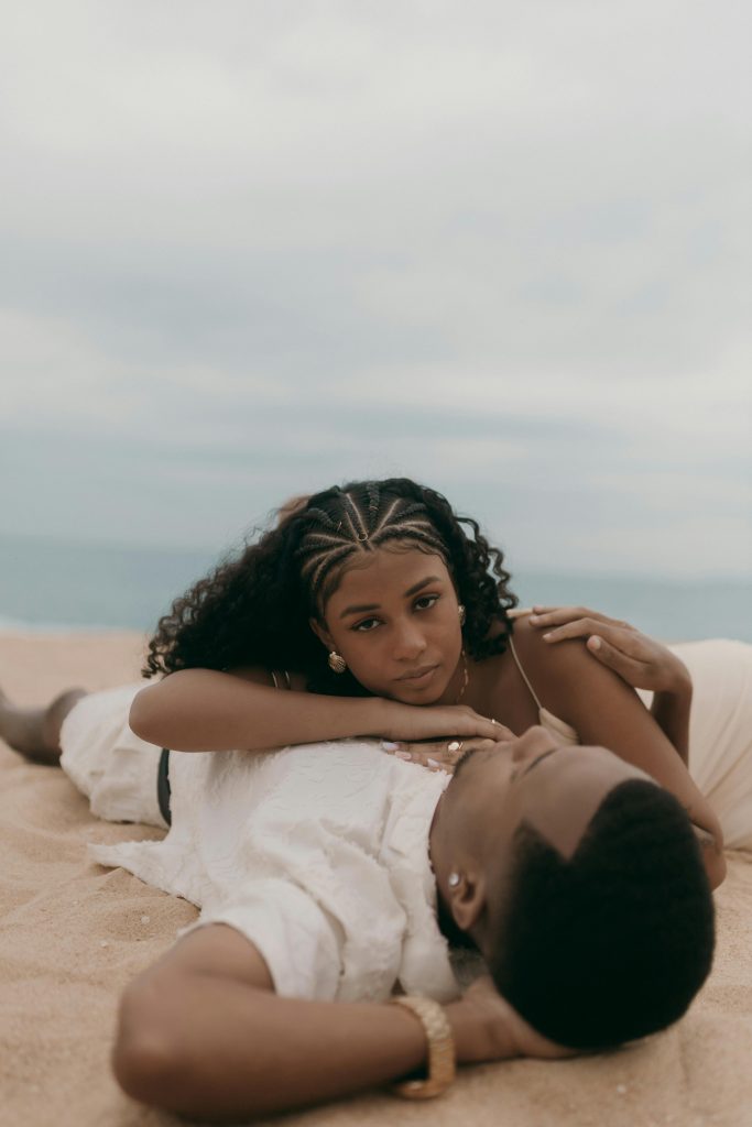 A young couple enjoys a relaxing moment on a sandy beach with the ocean in the background.