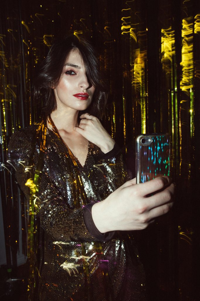 Stylish woman in gold attire using smartphone at a festive indoor event.