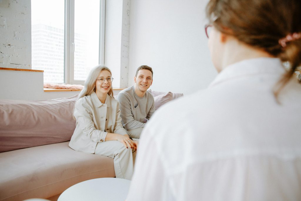 A couple smiles while sitting on a sofa during a counseling session indoors.