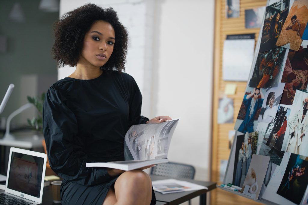 Elegant woman in a black dress holding a magazine in a modern office environment.