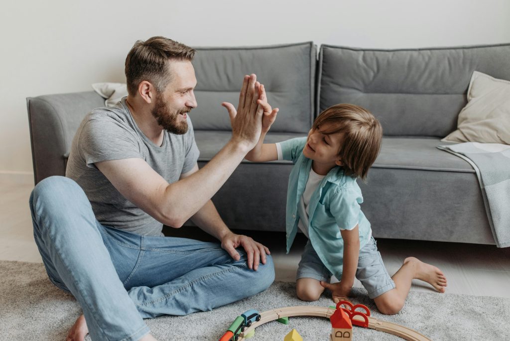 A father and son share a joyful high five while playing together indoors.