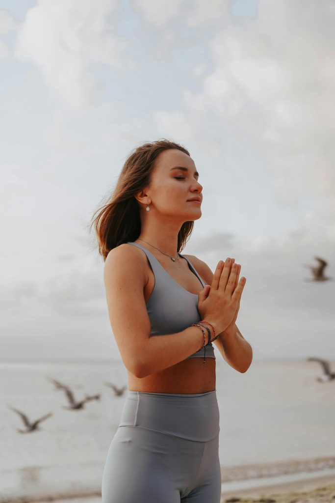 A woman in activewear meditates peacefully on a beach, embodying relaxation and mindfulness.